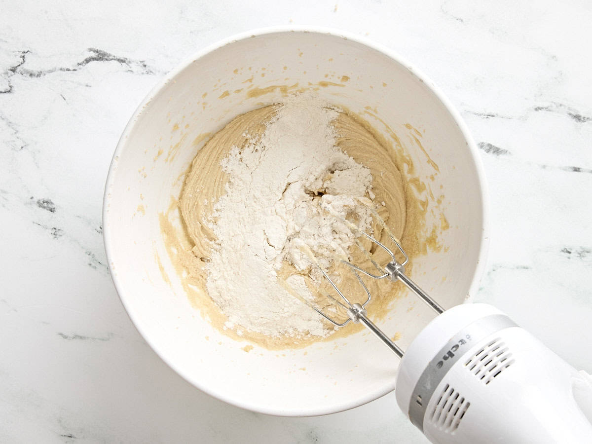 Flour being whisked by a hand mixer into wet ingredients for chocolate chip cookies.