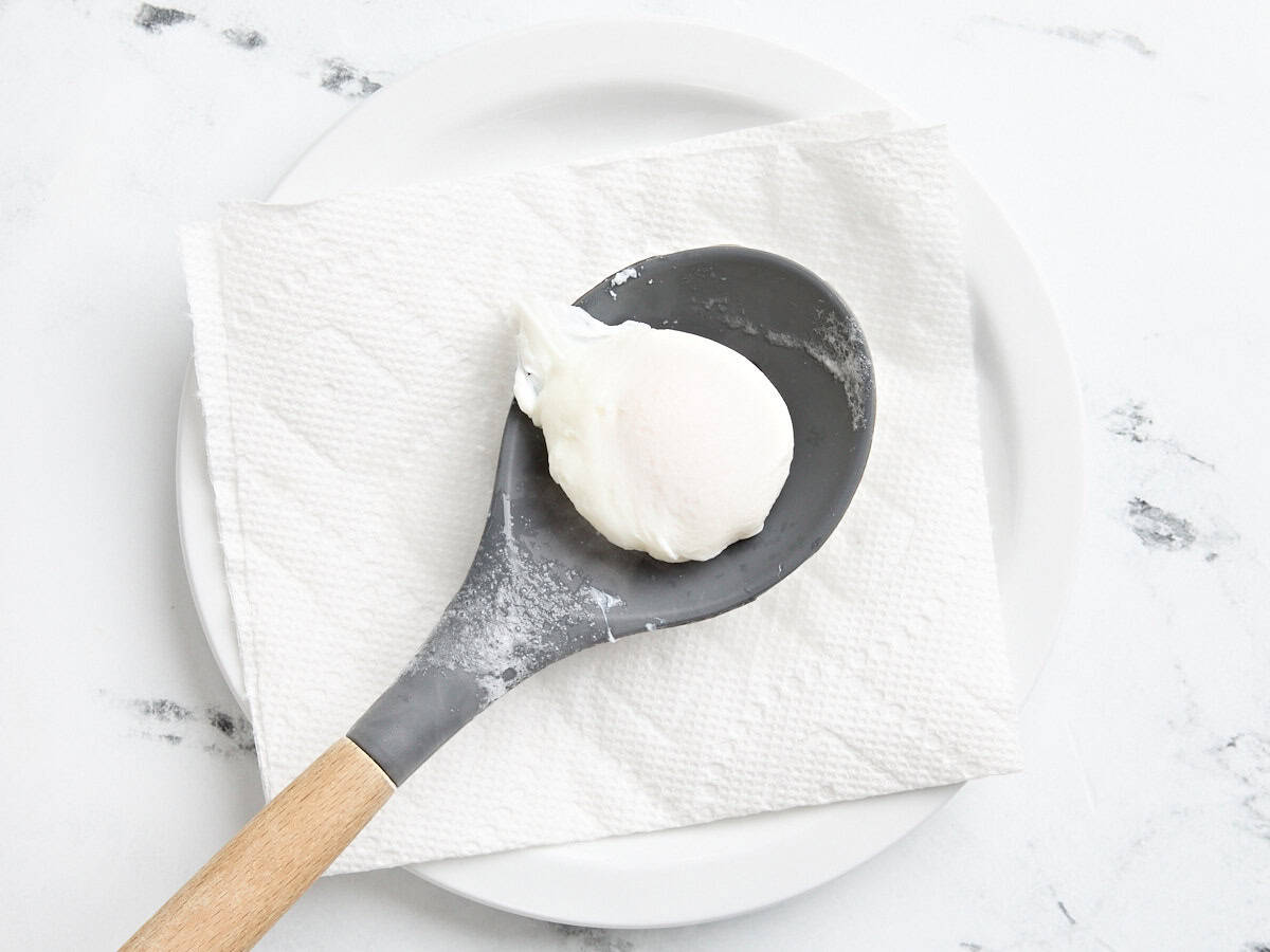 A finished poached egg on a plate with a piece of paper towel and a slotted spoon.