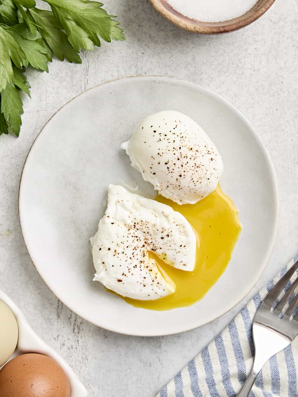 Overhead view of two poached eggs on a plate, with one cut open and the yolk running from it.