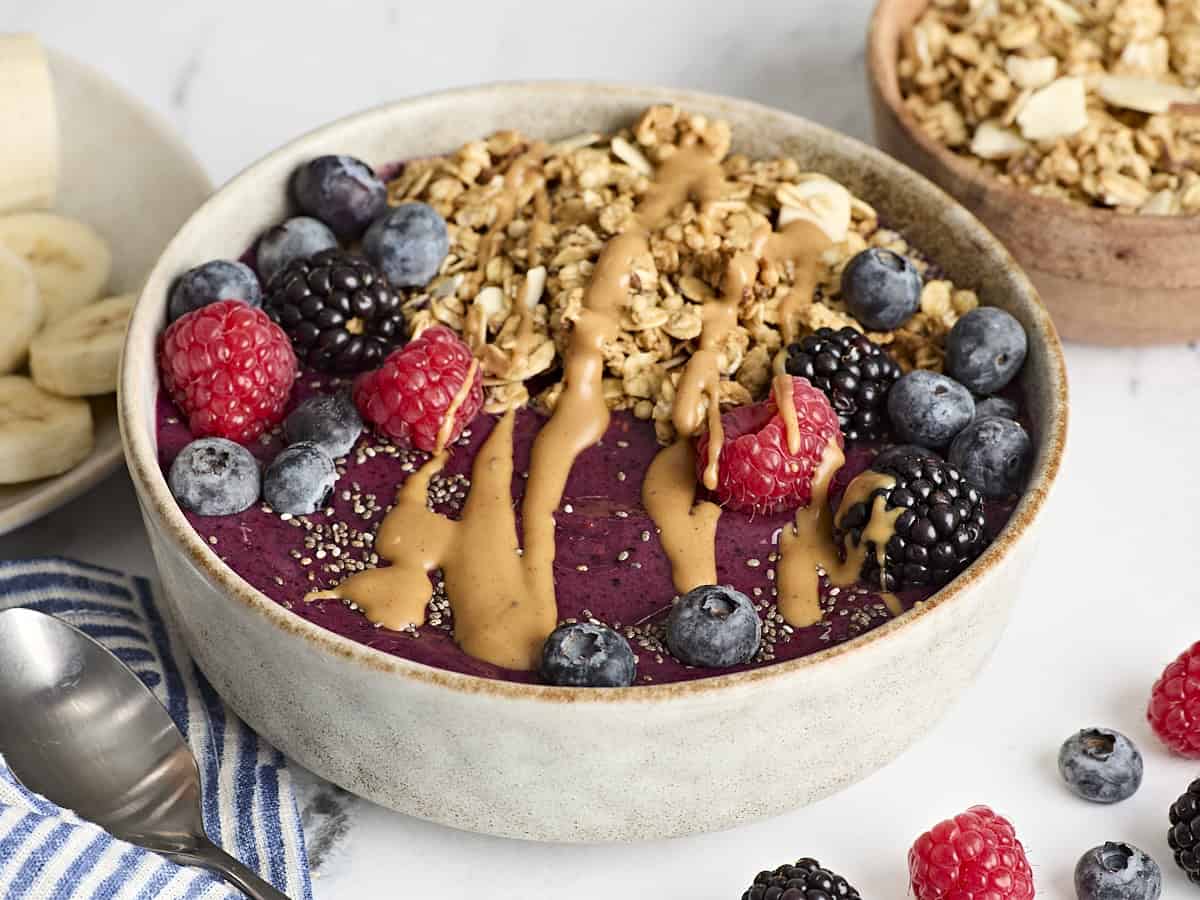 Side view of a smoothie bowl topped with granola, berries, peanut butter, and chia seeds.