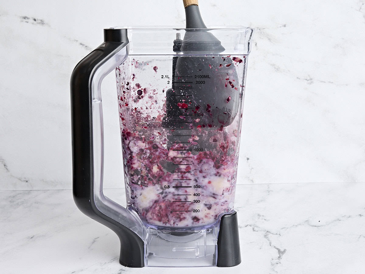 A spoon pushing down the filling for smoothie bowls in a blender halfway through blending.