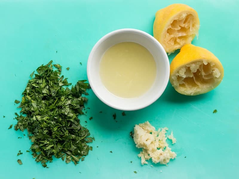 Overhead view of lemon juice, chopped parsley, and minced garlic.