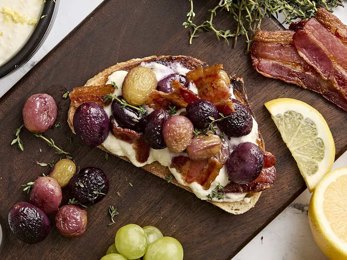 Overhead view of ricotta toast with roasted grapes, thyme and bacon.