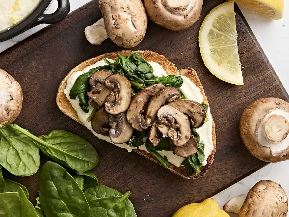 Overhead view of ricotta toast with mushrooms, garlic, wilted spinach, and red pepper.