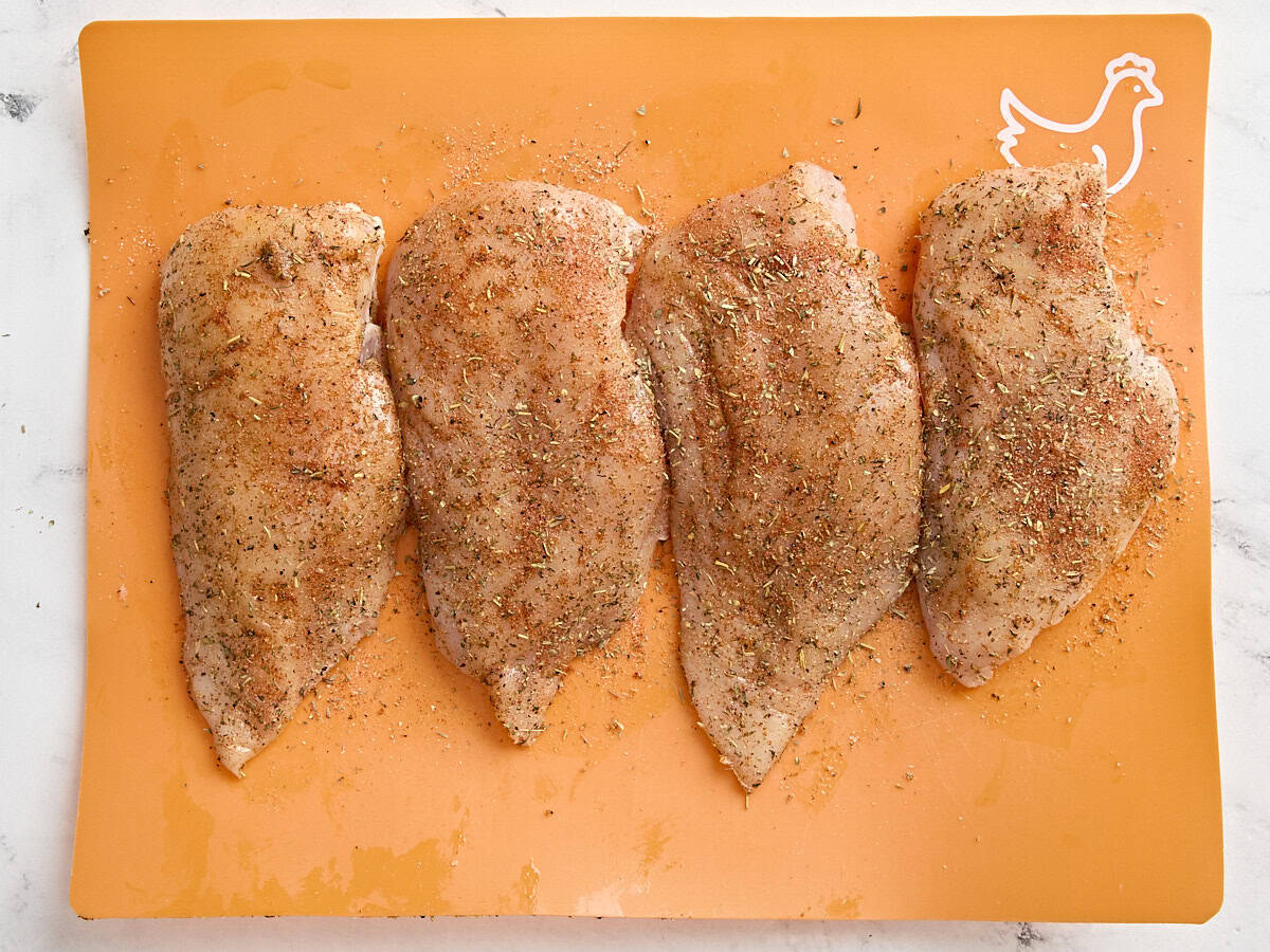 Seasoned chicken breasts on a meat preparation mat.