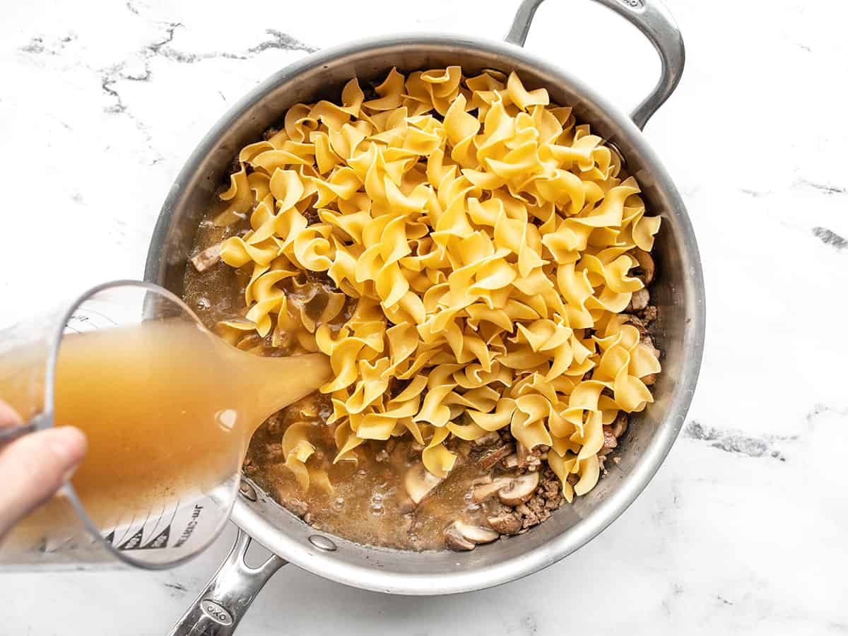 noodles added to the skillet, beef broth being poured in