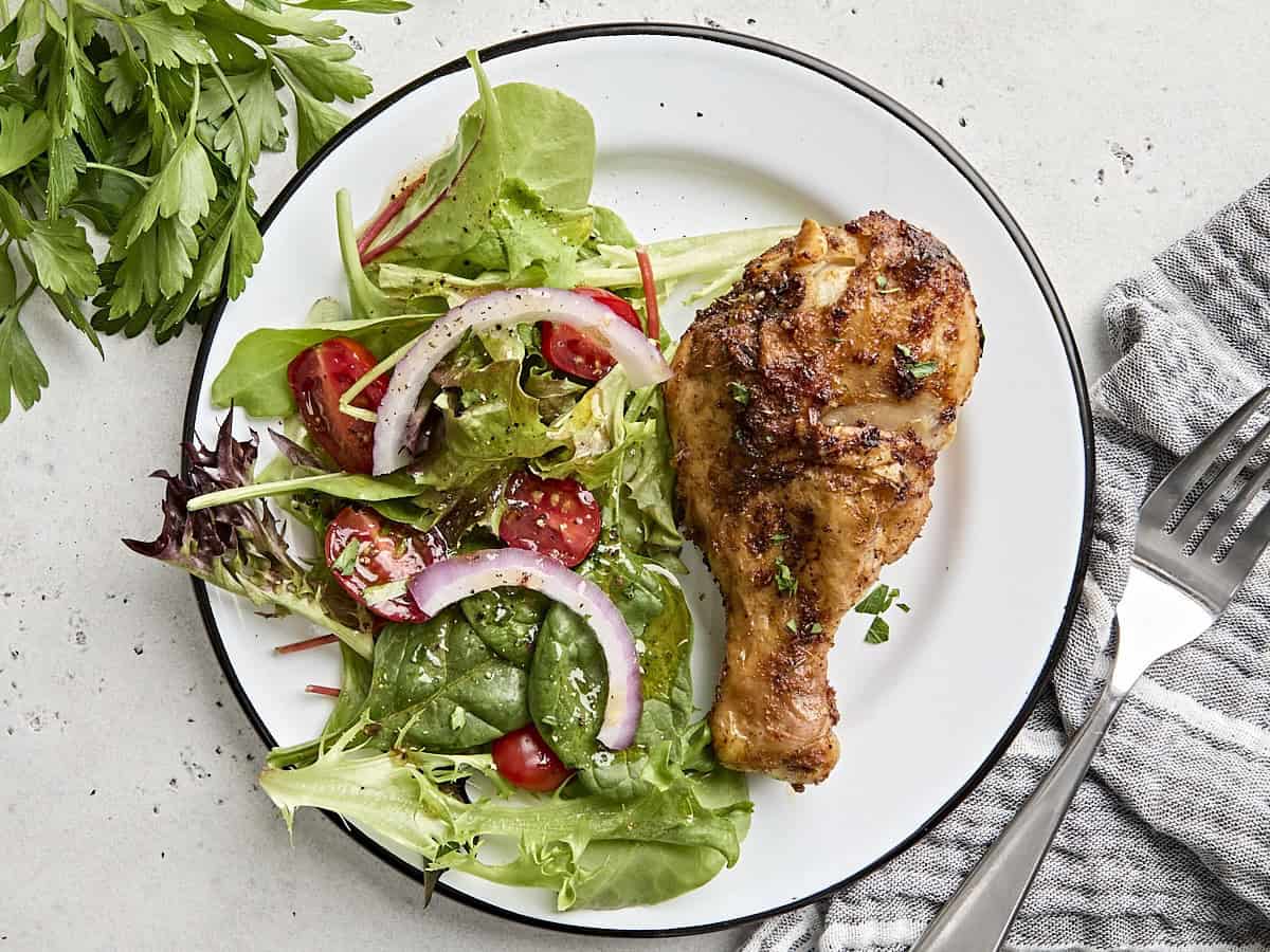 Overhead view of an air fryer chicken drumstick on a plate with a simple side salad.