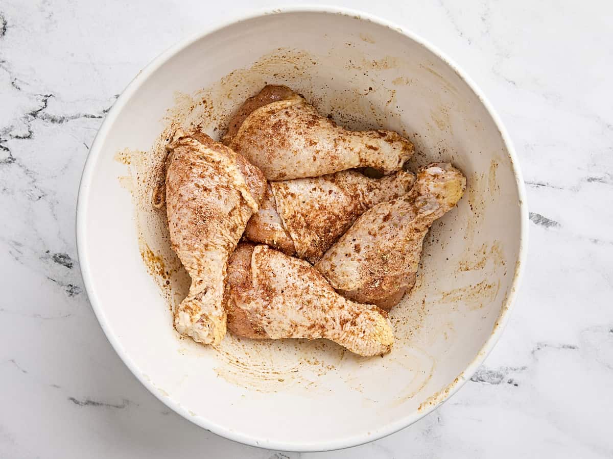 Seasoned chicken drumsticks in a bowl before air frying.